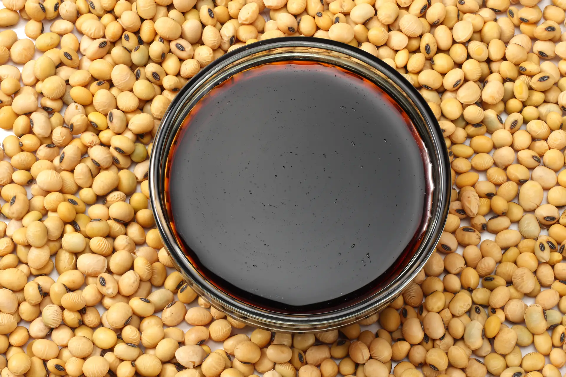 Soybeans background with soy souce in glass bowl. top view